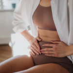 Mulher com dor abdominal segurando a região do baixo ventre, ilustrando sintomas da endometriose intestinal.